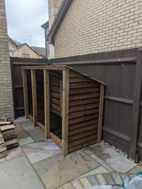 8ft wooden log Holton store with slanted roof and open front for firewood.