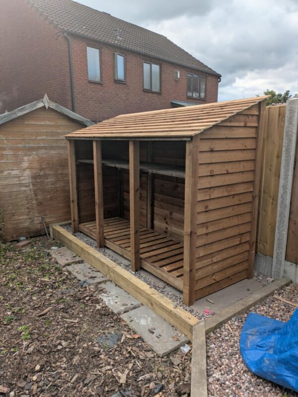 9ft deep log store Lavenham with 930mm depth, angled side view, triple bay wooden firewood store with slatted design.